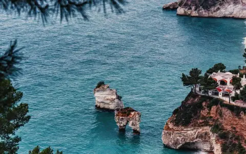 Scogliere mozzafiato e spiagge deserte Italia, con faraglioni che emergono dal mare turchese e una villa panoramica.