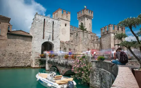 Castello Scaligero di Sirmione, un'ottima idea per cosa vedere a Sirmione in un giorno. Un ponte pedonale affollato porta all'ingresso del castello, con un motoscafo ormeggiato nell'acqua turchese.