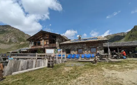 Rifugio Mont Fallère, uno dei rifugi Valle d'Aosta facili, accoglie escursionisti con le sue strutture in pietra e legno, circondato da verdi pendii e montagne.
