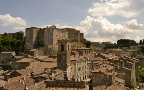 Panoramica di antichi borghi vicino Follonica, con un imponente castello in cima alla collina e un campanile che svetta tra i tetti rossi.