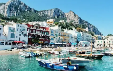 Colorate case affacciate sul mare turchese, con barche ormeggiate e montagne sullo sfondo. Un incantevole scorcio delle isole vicino Napoli.