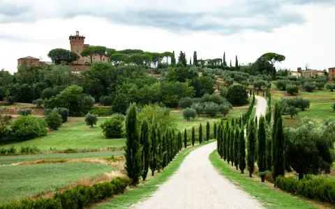 Un suggestivo itinerario Val d'Orcia 2 giorni: strada bianca tra cipressi e colline verdi, con un borgo in lontananza.
