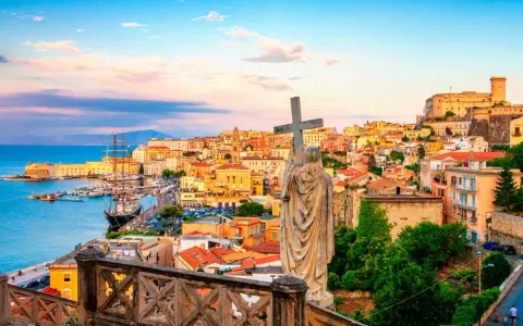 Una statua con una croce domina la vista di una città costiera colorata, perfetta per una gita fuori porta da Roma.