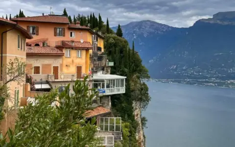 Case colorate aggrappate alla roccia a Tremosine sul Garda, con il lago e le montagne sullo sfondo.