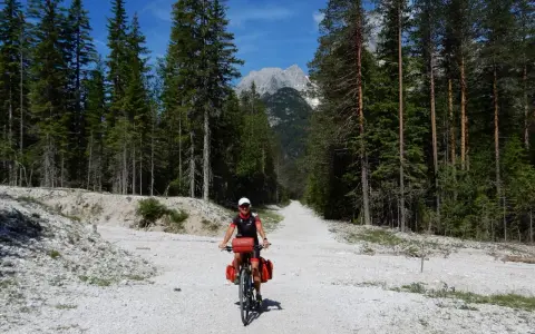 Ciclista su strada sterrata tra i pini, con le vette delle Dolomiti sullo sfondo. Un'avventura sui percorsi bici Dolomiti.