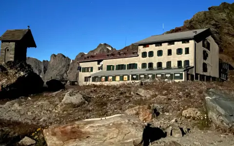 Rifugio alpino con piccola cappella, un esempio di cosa vedere in Lombardia, immerso in un paesaggio roccioso sotto un cielo stellato.