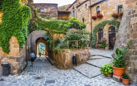 Un vicolo acciottolato tra antichi borghi da visitare nelle Marche, con case in pietra ricoperte di edera e fiori colorati.