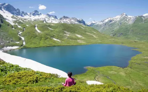 Pace e natura in Valle d'Aosta in estate: un lago alpino azzurro circondato da montagne innevate e verdi pascoli.