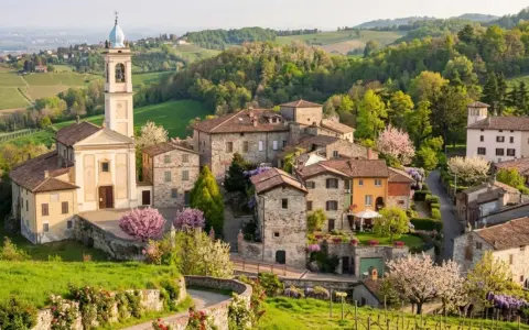 Borgo pittoresco con chiesa e campanile, colline verdi e fiori in primavera. Un luogo incantevole per scoprire cosa vedere a Golferenzo.