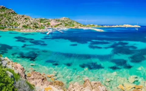 Acque cristalline e rocce granitiche ti aspettano per una visita alla Maddalena. Un paradiso azzurro con barche all'ancora.