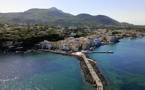 Ischia vista da Napoli: un borgo colorato si affaccia sul mare blu, con montagne verdi sullo sfondo.