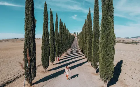 Viale di cipressi nel Val d'Orcia, un'icona da vedere in 3 giorni. Una donna cammina lungo la strada sterrata.