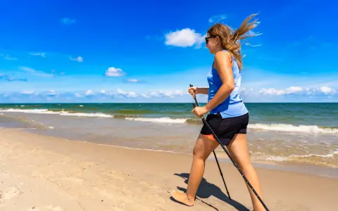 Donna con bastoncini da nordic walking in una splendida passeggiata al mare, con il vento che le scompiglia i capelli.