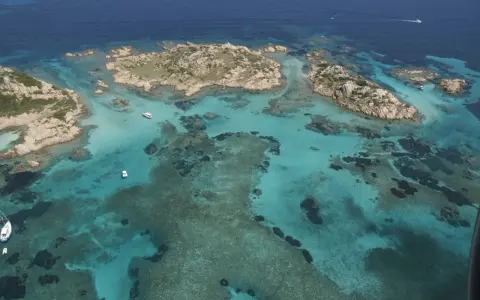Acque cristalline e isolotti rocciosi, un paradiso dove si trova la Maddalena. Barche navigano in questo mare turchese.