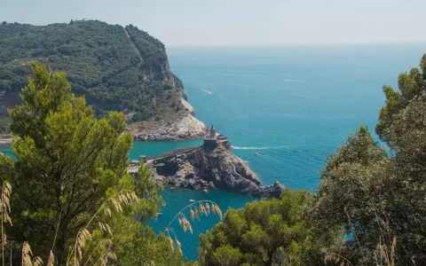 Vista panoramica del sentiero Riomaggiore Portovenere, con la chiesa di San Pietro su uno sperone roccioso e il mare azzurro.