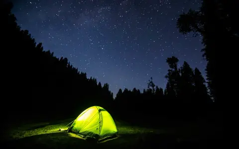 Tenda illuminata nella notte stellata, un invito a dormire in tenda immersi nella natura.