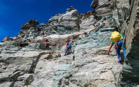Alpinisti scalano la roccia sul Monviso, seguendo la via normale. Un'avventura sotto il cielo azzurro.