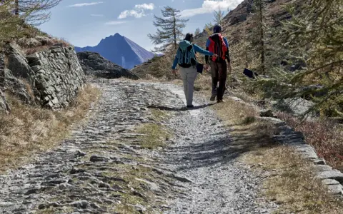 Escursionisti su sentiero sassoso nel Val di Susa, con montagne sullo sfondo.
