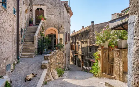 Un gatto si gode il sole in un vicolo acciottolato, tra antiche case di pietra e scale ripide. Un'atmosfera autentica di borghi da visitare nel nord Italia.
