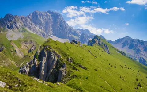 Prati verdi e sentieri invitano a **passeggiate facili** in Val Seriana, con maestose cime sullo sfondo sotto un cielo azzurro.