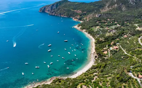 Baia con acque cristalline e numerose barche, incastonata tra colline verdi e scogliere. Un vero gioiello tra le spiagge più belle Toscana.