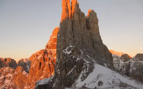 Le Torri del Vajolet illuminate dal caldo bagliore del tramonto, con la neve che ricopre le cime rocciose.