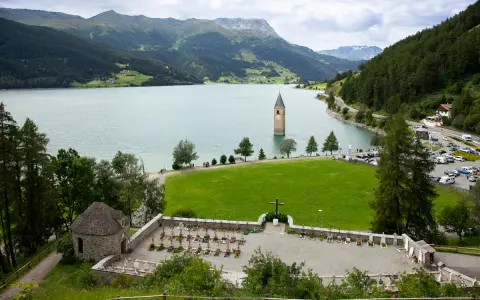 Un antico campanile nel lago, circondato da montagne verdi e un cimitero.