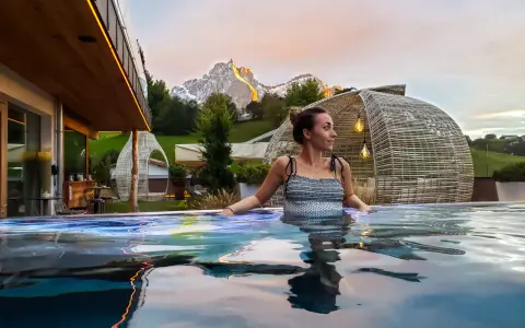 Donna rilassata in una piscina a sfioro con vista sulle montagne illuminate al tramonto, un'esperienza di benessere nelle terme in Trentino Alto Adige.
