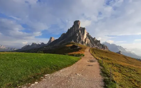 Sentiero per escursioni al Passo Giau, con imponenti vette rocciose e un rifugio alpino.