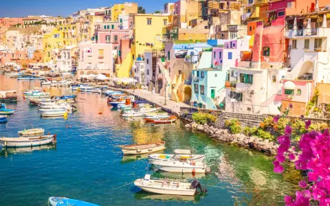 Porto di Corricella a Procida, un gioiello colorato. Ecco cosa vedere a Procida in un giorno: case pastello, barche nel blu intenso e bouganville in fiore.