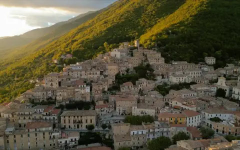 Borgo San Donato, un incantevole paese arroccato su un colle, immerso nel verde di una montagna illuminata dal sole al tramonto.