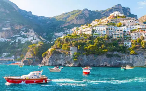 Barche a vela navigano nelle acque turchesi davanti alle case colorate aggrappate alle scogliere delle isole costiera amalfitana.