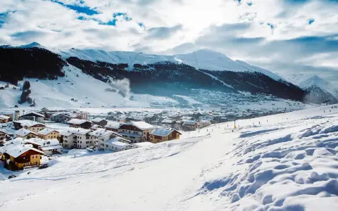 Paesaggio invernale con villaggio innevato e montagne sullo sfondo. Perfetto per sapere dove andare in montagna in Trentino per sciare.