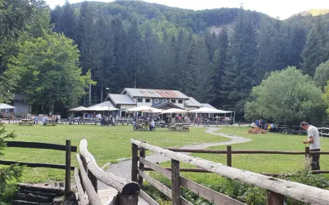 Un rifugio in Emilia Romagna immerso nel verde, con tavoli all'aperto e persone che si godono la giornata.