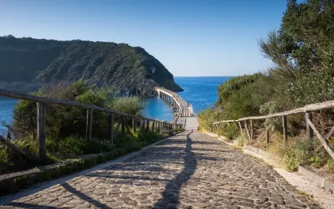 Sentiero acciottolato verso un ponte sul mare, ideale per cammini in Italia sul mare.