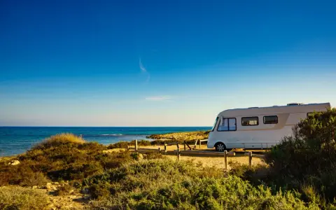 Un camper bianco sosta su un sentiero sabbioso con vista sul mare blu intenso. Un'avventura indimenticabile in camper all'Isola d'Elba.