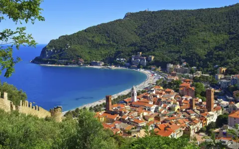 Vista panoramica di pittoreschi liguria paesi sul mare, con case dai tetti rossi che scendono verso una baia azzurra e una spiaggia affollata.
