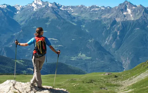 Escursionista con zaino e bastoncini ammira un panorama alpino mozzafiato, perfetto per scoprire gli itinerari della Valle d'Aosta.