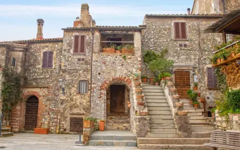 Antica piazza con case in pietra, scale in terracotta e piante rigogliose, un'atmosfera da **borghi medievali toscana**.