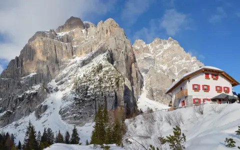 Rifugio alpino innevato ai piedi di maestose vette rocciose, un vero spettacolo di posti belli in montagna Veneto inverno.