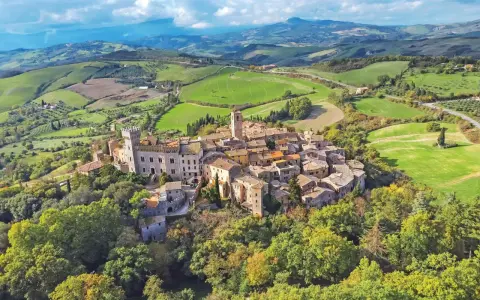 Un borgo medievale arroccato su una collina, circondato da dolci colline verdi. Un esempio dei borghi più belli della Toscana.