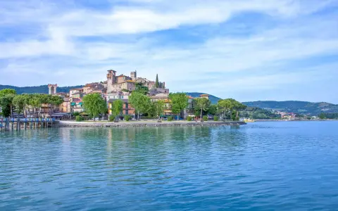 Il borgo più bello del Lago Trasimeno, con le sue case colorate e torri medievali, si specchia nelle acque azzurre.