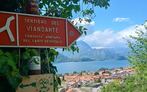 Segnale arancione indica "Sentiero del Viandante" con vista su un lago e montagne.