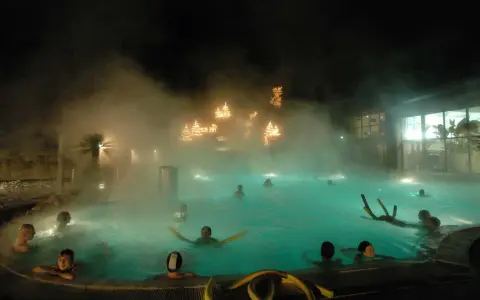 Persone si rilassano in una piscina termale notturna, con luci natalizie che brillano tra la nebbia, un'atmosfera magica nei bagni di Romagna.
