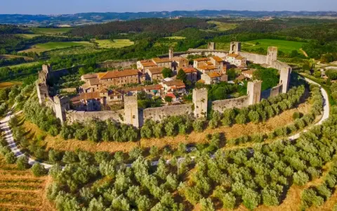 Borghi medievali fortificati vicino Siena, con mura imponenti e torri che dominano un paesaggio collinare verdeggiante.
