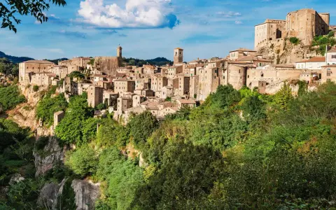 Un affascinante borgo toscano da visitare, arroccato su una rupe tufacea, con case in pietra e torri che si stagliano contro il cielo azzurro.