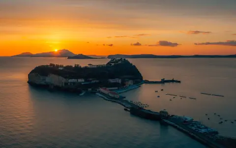 Tramonto infuocato sul golfo di Napoli, con una suggestiva isoletta che emerge dal mare calmo, illuminata dagli ultimi raggi dorati.