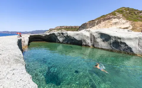 Un uomo nuota in acque cristalline tra scogliere bianche. Un luogo ideale per scoprire le spiagge di Bosa e cosa vedere.