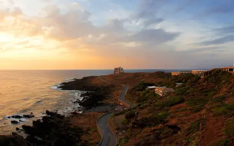 Torre di tramontana e case sparse su una collina, con mare e cielo al tramonto. Ecco cosa vedere a Ustica per un'esperienza indimenticabile.