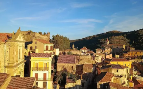 Panoramica di Castiglione di Sicilia al tramonto, con case dai tetti rossi e un castello in rovina su una collina.